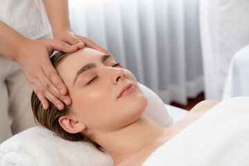 Caucasian woman enjoying relaxing anti-stress head massage and pampering facial beauty skin recreation leisure in dayspa modern light ambient at luxury resort or hotel spa salon. Quiescent