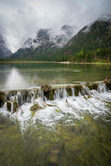 Alpine lake Lago di Dobbiaco in Dolomites mountains, Cortina dAmpezzo, Italy on moody spring day. Lake Toblacher See in the forest in Dolomiti in Italian Alps