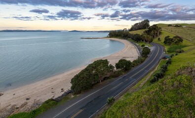 Beach coastline, coastal road and farmland along the Firth of Thames at sunset. Maraetai, Auckland, New Zealand.