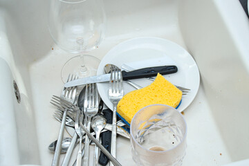 Close up of white ceramic kitchen sink full with dirty unwashed dishes 