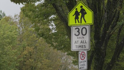 School zone traffic sign, 30 km/h speed limit, cloudy rainy day, quiet neighborhood, green trees