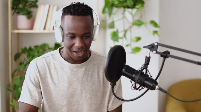 Happy young african man making audio podcast from home. Content creator recording radio show using professional microphone at small broadcast studio