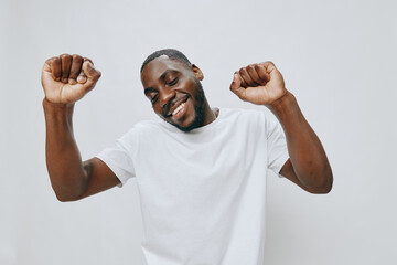 Happy young man celebrating in a bright white t shirt, expressing joy and positivity against a light grey background, embodying success and enthusiasm