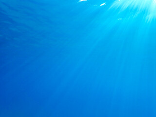 Dark blue ocean surface seen from underwater. Abstract waves underwater and rays of sunlight shining through, Sun light rays undersea deep, Underwater background with sea bottom, Mediterranean sea.