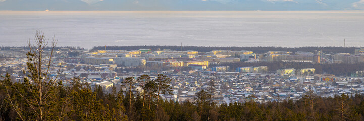 Severobaikalsk, Republic of Buryatia, Siberia, Russia. View of the city of Severobaikalsk, located on the coast of Lake Baikal. Winter city landscape. Lake Baikal is covered with ice. Wide panorama.