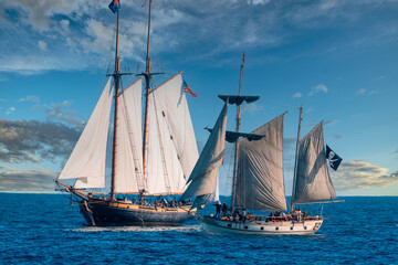 Tall ships sailing in the Pacific ocean during the afternoon carrying passengers on a cruise.