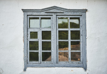 Close-up of an old grey wooden window on a white wall. Part of an old house with painted and weathered window