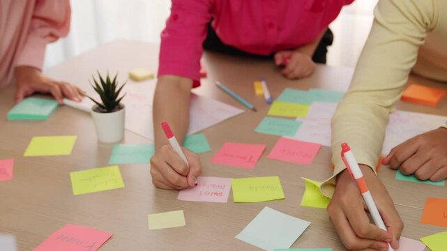 Slow motion hand closeup of startup employee team brainstorming strategic marketing plan and making mind map with colorful sticky notes placed on office table at meeting room. Variegated