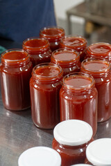 Jars of freshly made rosehip jam in an artisan factory. The jam, rich in color and texture, fills the glass jars to the brim, ready for sealing. Captured during production