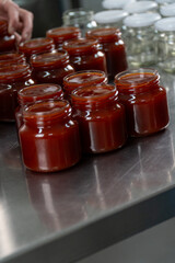 Jars of freshly made rosehip jam in an artisan factory. The jam, rich in color and texture, fills the glass jars to the brim, ready for sealing. Captured during production