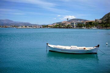 Naklejka premium small white boat anchored in a bay with turquoise blue water in nafplio in greece on a sunny summer day