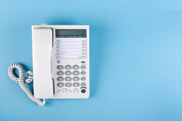 White telephone with handset on light blue background, top view. Space for text