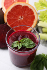 Tasty beetroot smoothie with basil in glass, fresh vegetables and grapefruits on light table, closeup. Vegan drink