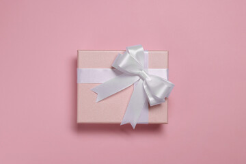 Gift box with bow on dusty pink background, top view