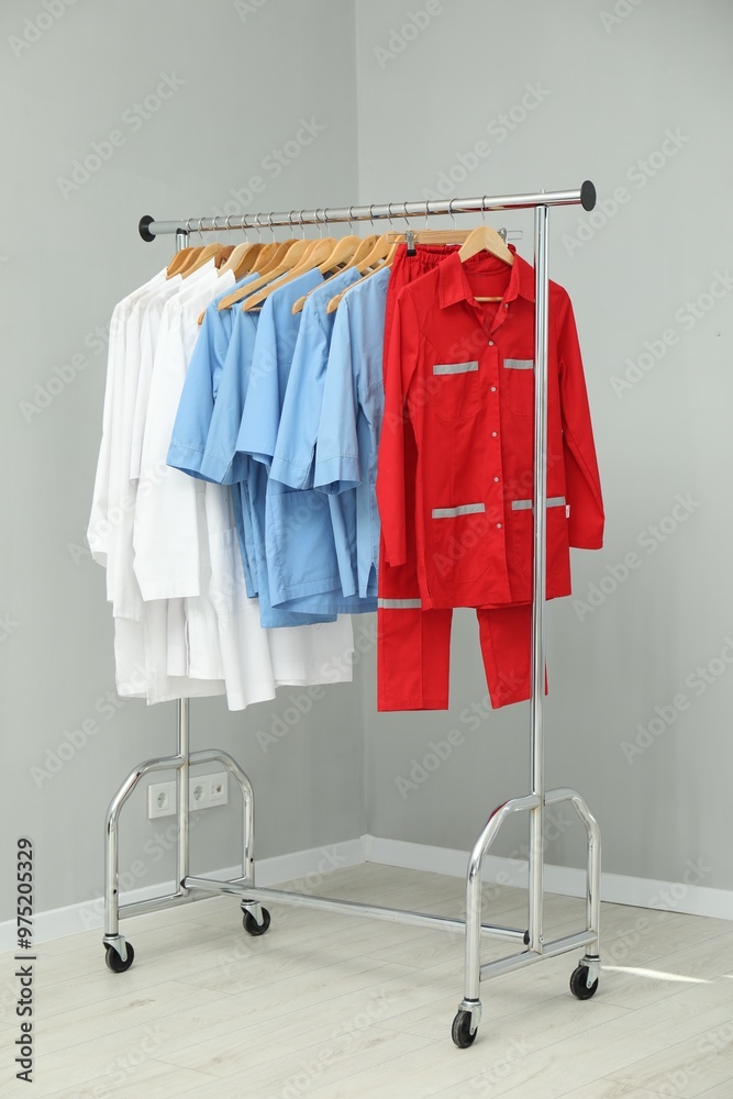 Wall mural Different medical workers' uniforms on clothing rack near grey wall indoors