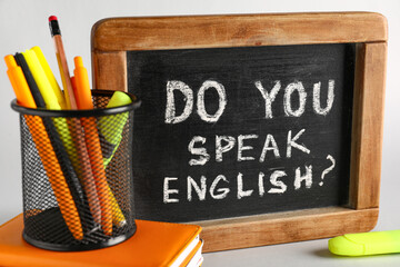 Stationery and blackboard with question DO YOU SPEAK ENGLISH? on grey background