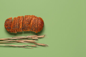 Loaf of sliced rye bread and wheat ears on green background