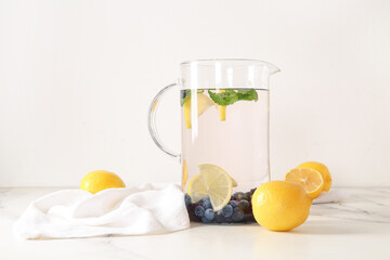 Jug of infused water with blueberries, blackberries and lemon on white background