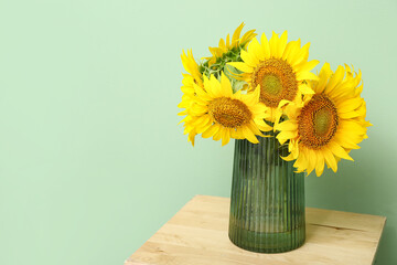 Vase with sunflowers on stool near green wall
