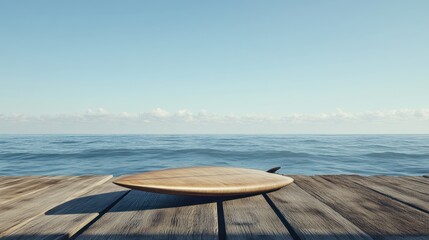 A wooden surfboard rests on a dock overlooking calm ocean waters under a clear sky.
