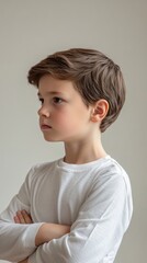 Side profile of young boy with crossed arms in white shirt, studio portrait. Childhood and innocence concept