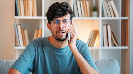 Confusing call. Mobile scam. Skeptic dissatisfied shocked puzzled man speaking on phone at modern...