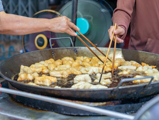 Two vendor uses chopsticks to flip the deep-fried dough sticks.
