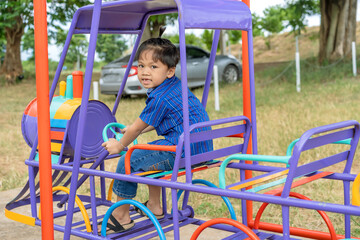 Portrait of a cute little Asian boy. Sitting on play equipment at school or kindergarten or playground. Summer activities, outdoor play, happy, relaxing, and educational ideas.