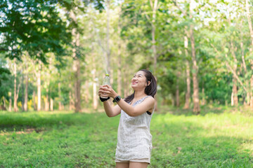 Obraz premium Happy young woman holding a water bottle in her hand Her cheerful demeanor and relaxed demeanor reflect the happiness she finds in her peaceful surroundings. Lifestyle of happiness.