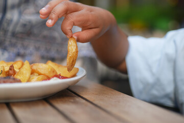 A child eagerly reaching for fries at an outdoor table, reflecting the joy of family meals