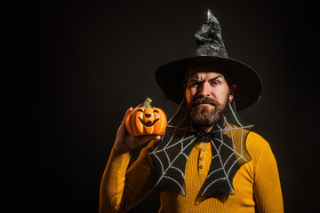 Funny model with Halloween pumpkin. Portrait of mature Man in Halloween hat with pumpkin. Trick or treat. Scary hipster with beard in Halloween hat. Man with witch hat hold pumpkin. Happy Halloween.