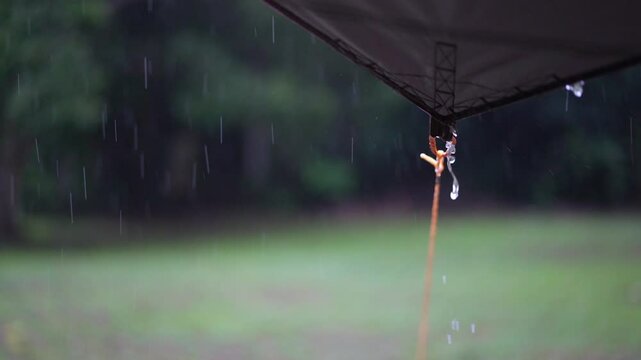 camping on rainy season with heavy rain water drips droplets to tip tarp and flow slow motion on fly sheet tent with carabiner paracord rope umbrella by holiday travel picnic on nature forest garden