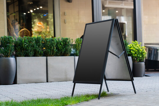 Empty A-frame sidewalk sign placed on city street, perfect for customizable advertising in front of a shop or café.