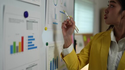 Female office worker, businesswoman standing in front of a whiteboard pointing at a graph, chart Information on marketing, finance, business growth Presenting information at office meetings.