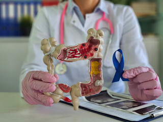 Healthcare professional explaining digestive health using a model and awareness ribbon in a...