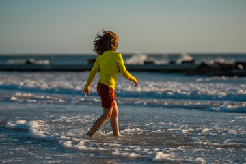 Carefree child running on sea. Happy cute child running near ocean on warm summer day. A Cute little kid boy running and splashing in sea or ocean on a family vacation. Kid running along the beach.