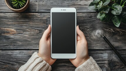 Person holding a white smartphone on a rustic wooden table, offering a top-down view of the device, ready for use.