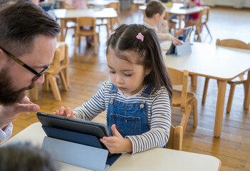 A young girl using a tablet with her teacher in a bright classroom, symbolizing technology and personalized learning.