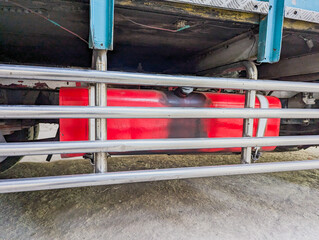 A close up view of the undercarriage of a vehicle, focusing on a red fuel tank, the tank is secured by metallic bar guards, logistic vehicle.