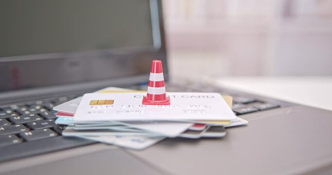 Household and credit card debt, personal loan, payment overdue, financial problems : Traffic warning cone atop a stack of credit cards on a laptop, depicting problems in repaying credit card debt.