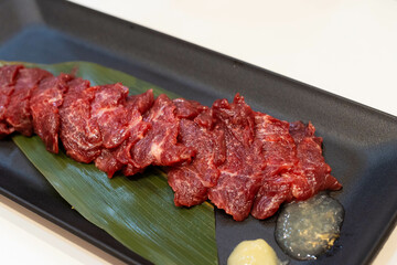 Basashi or raw horse meat sashimi with garlic and ginger sauce on black plate with white background, famous dish of Kumamoto, Japan