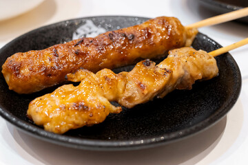 Assorted yakitori or grilled chicken skewers on black plate in izakaya restaurant