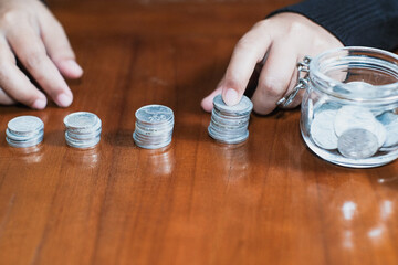 The piles of coins and coins on the glass jar on the table with the hand held the coins save money in the future, Savings and investing concept.