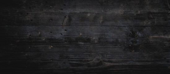 Rustic, dark wood surface aged texture showcases intricate grain patterns. Charred and weathered, planks reveal vintage, earthy warmth, creating natural, organic feel reminiscent of firewood.