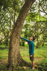 A man's hands gently touch the rough bark of a towering tree, symbolizing a deep connection with nature. In the forest, he embraces the importance of environmental care and protecting the planet.
