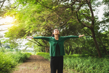 confident asian woman embraces self-love, standing peacefully in serene park at sunset. joyful smile, she enjoys fresh air, breathing deeply, radiates calm and positivity in tranquil surroundings.