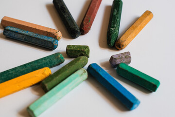 A collection of used, multi colored crayons or pastels arranged in a loose circular pattern on white background, likely for drawing or coloring.