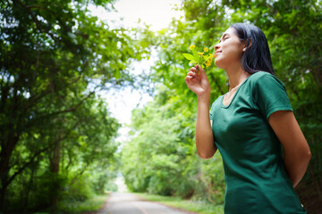 Obraz premium A cheerful young asian woman enjoys a sunny day outdoors, holding a vibrant bunch of yellow flowers. Smiling in a green field, she embodies the joy and freedom of summer in the countryside.