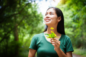 A cheerful young asian woman enjoys a sunny day outdoors, holding a vibrant bunch of yellow flowers. Smiling in a green field, she embodies the joy and freedom of summer in the countryside.