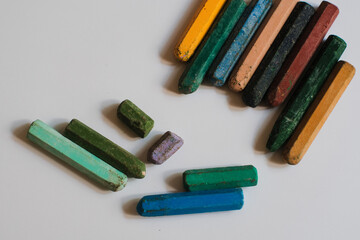 A set of multi colored crayons or pastels neatly aligned in a row on a white background, the materials are likely used for artistic purpose such as drawing or coloring.